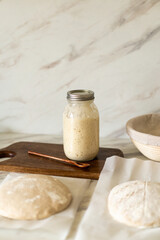 Freshly prepared sourdough bread dough rests on parchment near a container of active starter and a mixing bowl, showcasing the art of home baking.