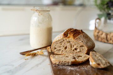 Crispy sourdough bread sits beside a glass jar filled with active starter, accompanied by a rustic...