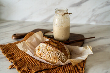 Crispy sourdough bread sits beside a glass jar filled with active starter, accompanied by a rustic...