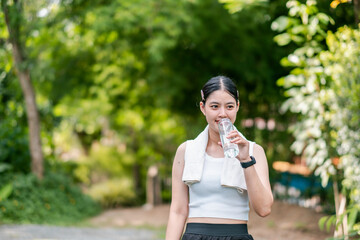 A woman takes a break during her workout, drinking water in a vibrant green park. Fitness and...
