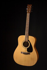 Naklejka premium acoustic guitar made of light wood on a black background. close-up.