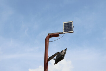 Solar panel mounted rusted metal pole with streetlight attached, set against clear blue sky,...