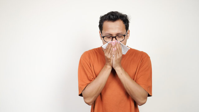 A man with glasses is blowing his nose with a tissue