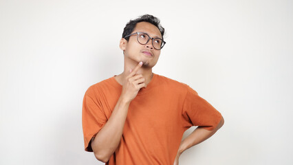 A man in an orange shirt is looking to the left with his hand on his chin