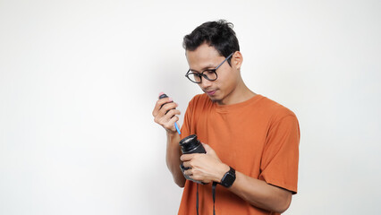 A man in an orange shirt is holding a camera lens.
