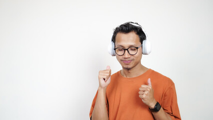 A man in an orange shirt is wearing headphones and talking on a cell phone