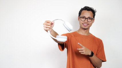 A man in an orange shirt is holding a white earbud and pointing to it