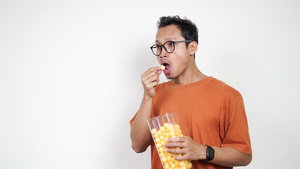 A man in an orange shirt is eating a bag of yellow snacks