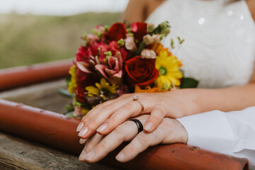 Close-up of bride and groom hands with engagement ring and wedding band resting on a wooden railing...