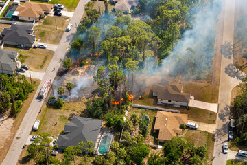 Firefighters battle a fast moving wildfire in Florida forest near suburban homes with fire trucks...