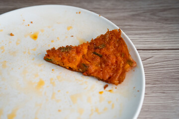 Telur dadar or omelet slice on a white plate with sauce stains, against a wooden table background. 