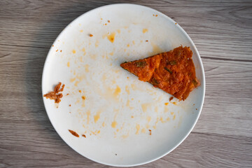 Telur dadar or omelet slice on a white plate with sauce stains, against a wooden table background. 