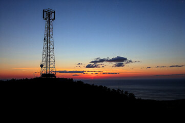 Obraz premium Coastal cell tower silhouetted against vibrant sunset