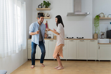 Happy couple dancing together barefoot in kitchen, enjoying fun and energetic moment in cozy modern home