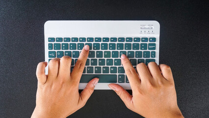 Top view of fingers typing on a green modern wireless computer keyboard isolated on black background
