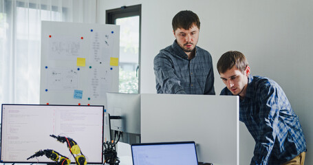 Team adult male engineer collaborate on robotic hand project using AI code solutions machine learning at tech workspace. Artificial intelligence interface, collaboration support prototype development.