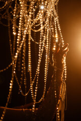 Female hand in lace glove touches crystal chandelier strands in dark room with warm light. Elegant, mysterious, festive. Concepts: luxury, celebration, elegance, mystery.