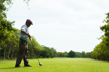 Elderly Asian man enjoying the morning round of golf in soft and warm sunlight.