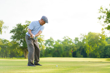 Elderly Asian man enjoying the morning round of golf in soft and warm sunlight.