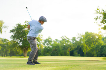 Elderly Asian man enjoying the morning round of golf in soft and warm sunlight.