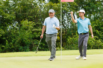 Asian man and elderly father are enjoy playing golf together with a good time.