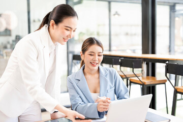 Two young asian businesswomen discussing work over laptop in office