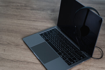 All center and customer service modern laptop with black screen and pair of headphones resting it, placed wooden surface, creating sleek workspace