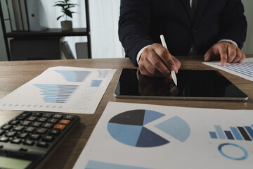 Report document person formal attire working with digital and printed data wooden desk, using tablet and stylus for analysis or presentation