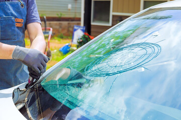 Technician works on fixing cracked windshield using specialized tools in driveway during glass replacement