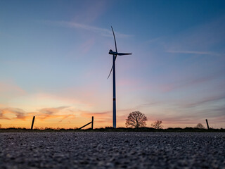 A wind turbine stands elegantly silhouetted against a vibrant sunset over a vast, beautiful...