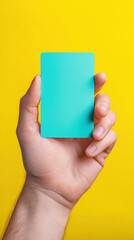 Hand holding blank turquoise unbranded card on vibrant yellow background