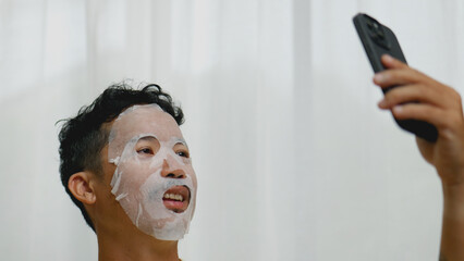 Asian man wearing sheet mask while video calling friends.