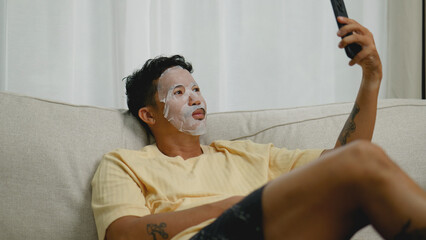 Asian man wearing sheet mask while video calling friends.