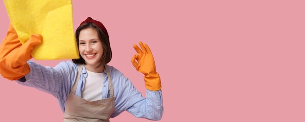 Young housewife with rag showing OK on pink background with space for text