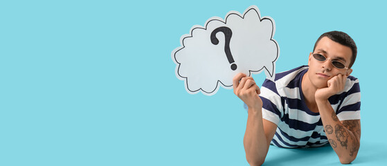 Young man holding paper with question mark on blue background