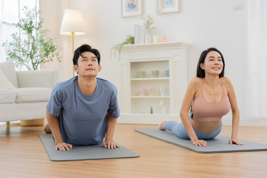 Asian Young couple practicing yoga together at home, smiling and enjoying healthy lifestyle in bright living room