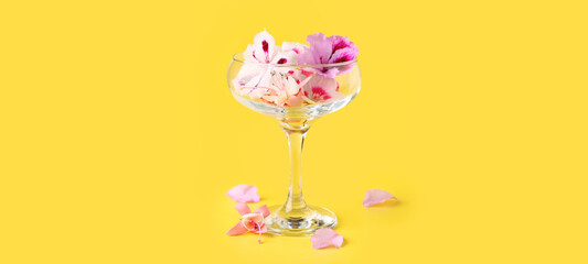 Glass with different beautiful edible flowers on yellow background