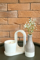 Gypsophila flowers and candle on table near brick wall in room, closeup