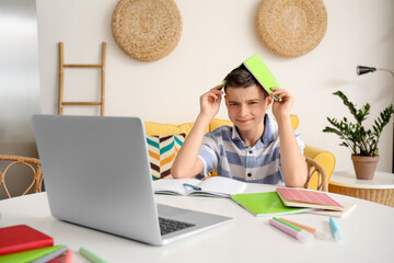 Tired little boy with copybook studying online at home