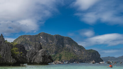 Many Filipino bangka boats are anchored in the turquoise lagoon. A tourist canoe is sailing....