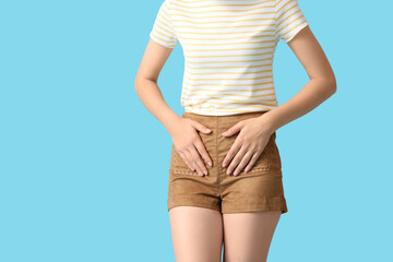 Young woman suffering from cystitis on blue background, closeup
