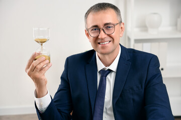 Mature businessman with hourglass in office, closeup