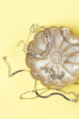 Plate with different stylish silver bracelets on yellow background