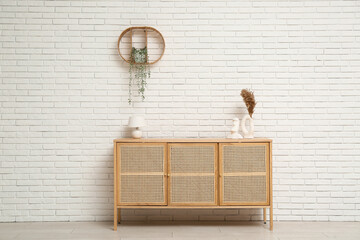 Modern light wooden chest of drawers with lamp and pampas grass in vase near white brick wall in...