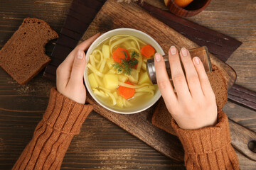 Woman adding spices into bowl with tasty chicken soup on wooden background