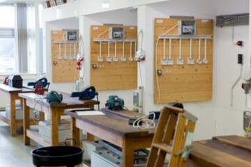 Wooden workbenches featuring bench grinders and loose cables are lining flat design workshop room