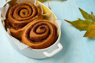Baking dish of tasty cinnamon rolls and autumn leaf on blue background