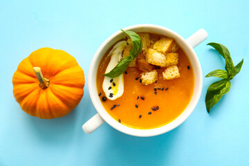 Pot of delicious pumpkin cream soup with croutons and basil on blue background