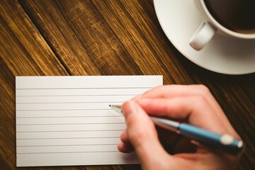 Human hand writing on paper at desk with coffee cup