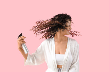 Beautiful African-American woman spraying hair on pink background